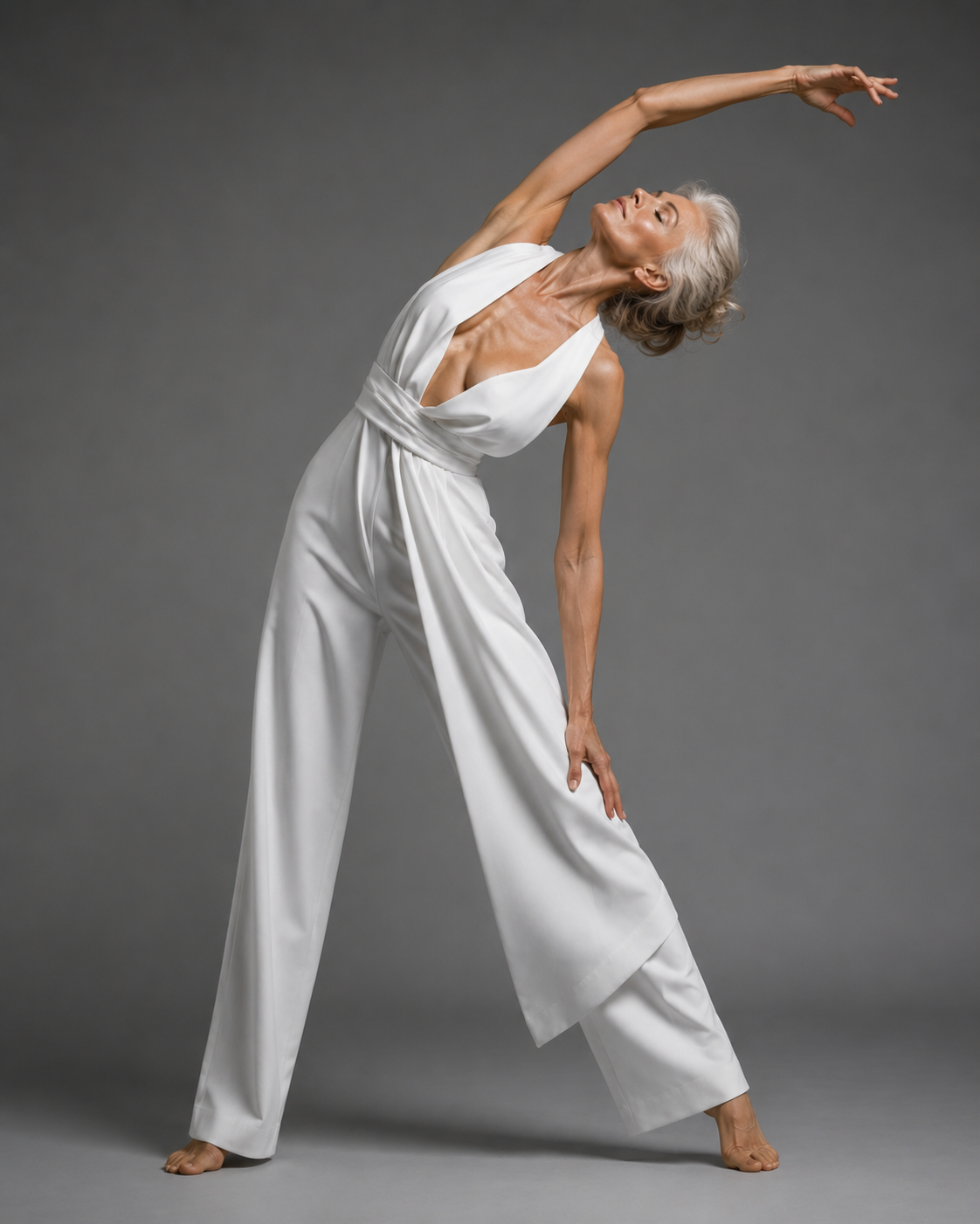 mature silver-haired woman, grey studio backdrop in white jumpsuit, arched back with arm extended, wide stance, expressive